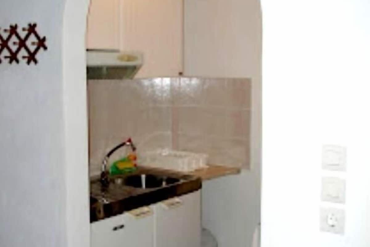 A narrow kitchen with white cabinets, a sink, and a tiled backsplash.