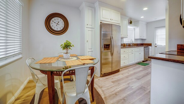 Una cocina con armarios blancos, un refrigerador de acero inoxidable y una mesa de comedor con sillas.