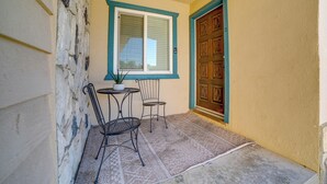 Un pequeño patio con una mesa y dos sillas, una ventana con persianas y una puerta con un panel decorativo.