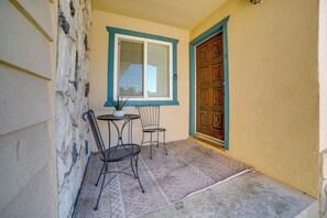 Ein kleiner Innenhof mit Tisch und zwei Stühlen, ein Fenster mit Jalousien und eine Tür mit einem Zierpaneel.