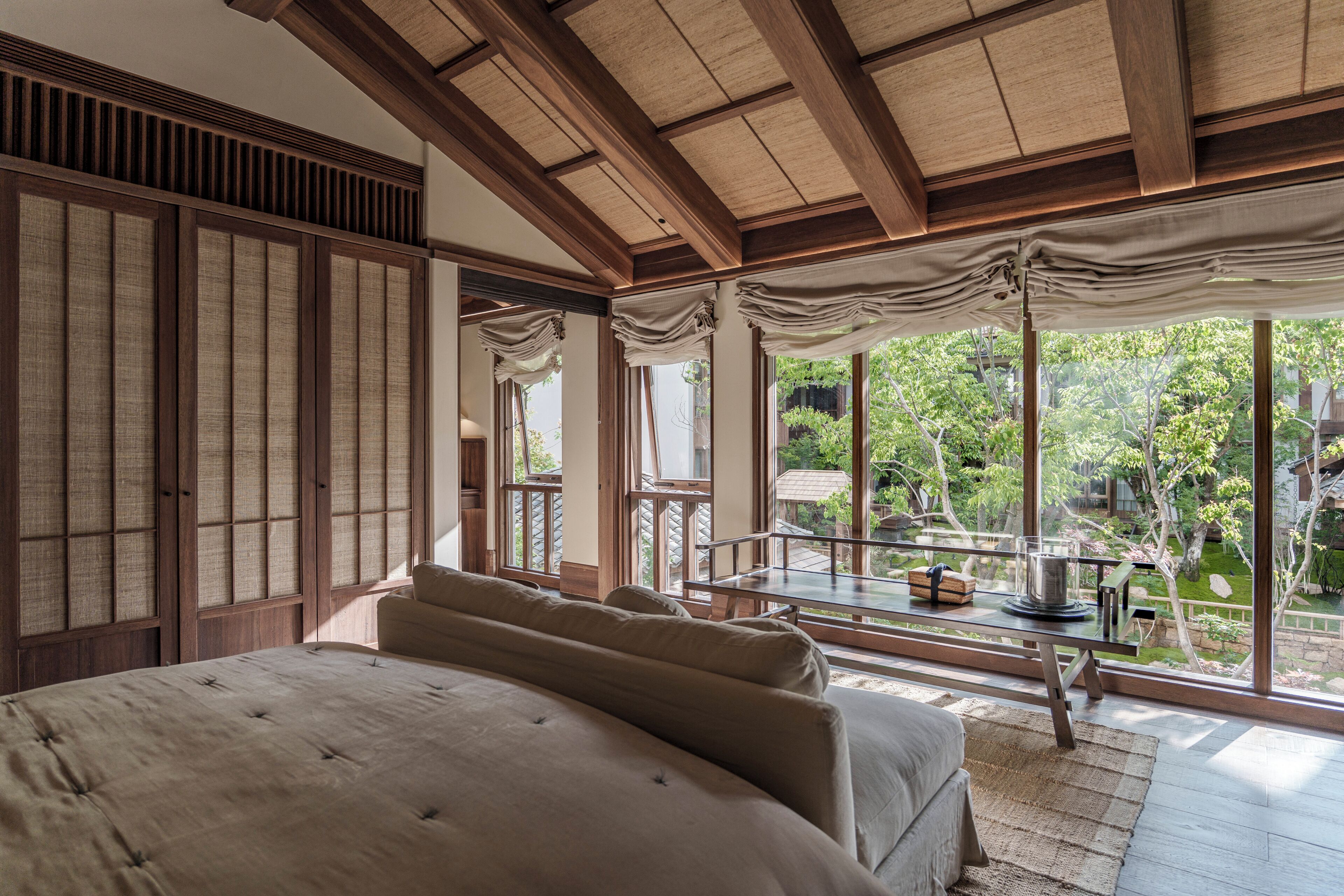 Una stanza tradizionale in stile giapponese, con pavimento in tatami, un letto basso in legno e vista su un giardino attraverso ampie finestre.