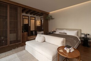Un dormitorio moderno con cama, sofá, una mesita con libros y una puerta corredera tradicional.