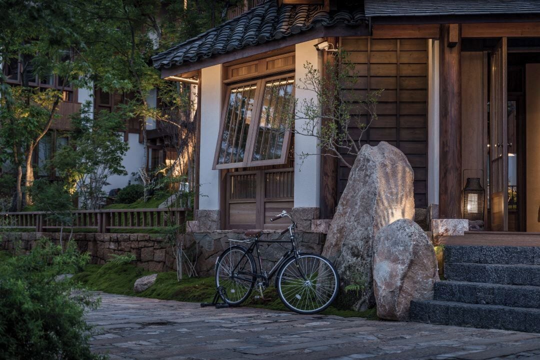 A traditional Japanese building with a bicycle, large rocks, and a stone pathway.