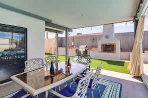 An outdoor patio with a glass table, blue cushioned chairs, a barbecue grill, and a decorative wall. - Game Room, Pool & Lake Fun at 'Indian Land Oasis' (Lake Havasu City)