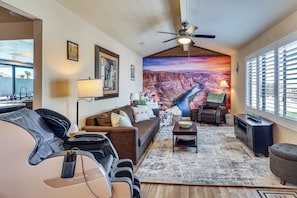 A living room with a sofa, a coffee table, a TV, a ceiling fan, and a large mural of a canyon. - Game Room, Pool & Lake Fun at 'Indian Land Oasis' (Lake Havasu City)