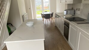 A modern kitchen with a central island, a dining area with chairs, and a view through a glass door. - House Sleeps 5 With Balcony (Hull)