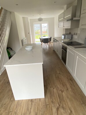 A modern kitchen with a central island, a dining area with chairs, and a view through a glass door.