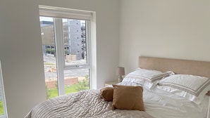 A bedroom with a large bed, a window with a view of buildings, and a pendant light. - House Sleeps 5 With Balcony (Hull)