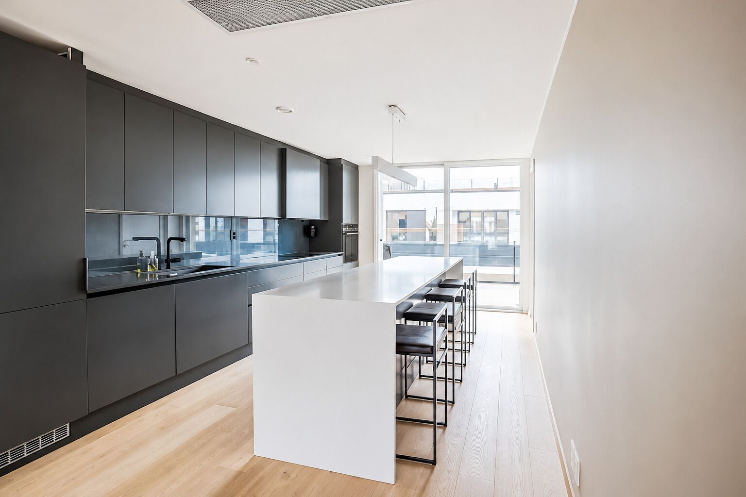 A modern kitchen with a central island, bar stools, and a view of the city through large windows.
