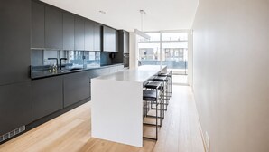 Une cuisine moderne dotée d’un îlot central, de tabourets de bar et offrant une vue sur la ville grâce à de grandes fenêtres.