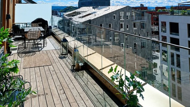 Une terrasse sur le toit offrant une vue sur les bâtiments modernes, avec une plateforme en bois et du mobilier d’extérieur.