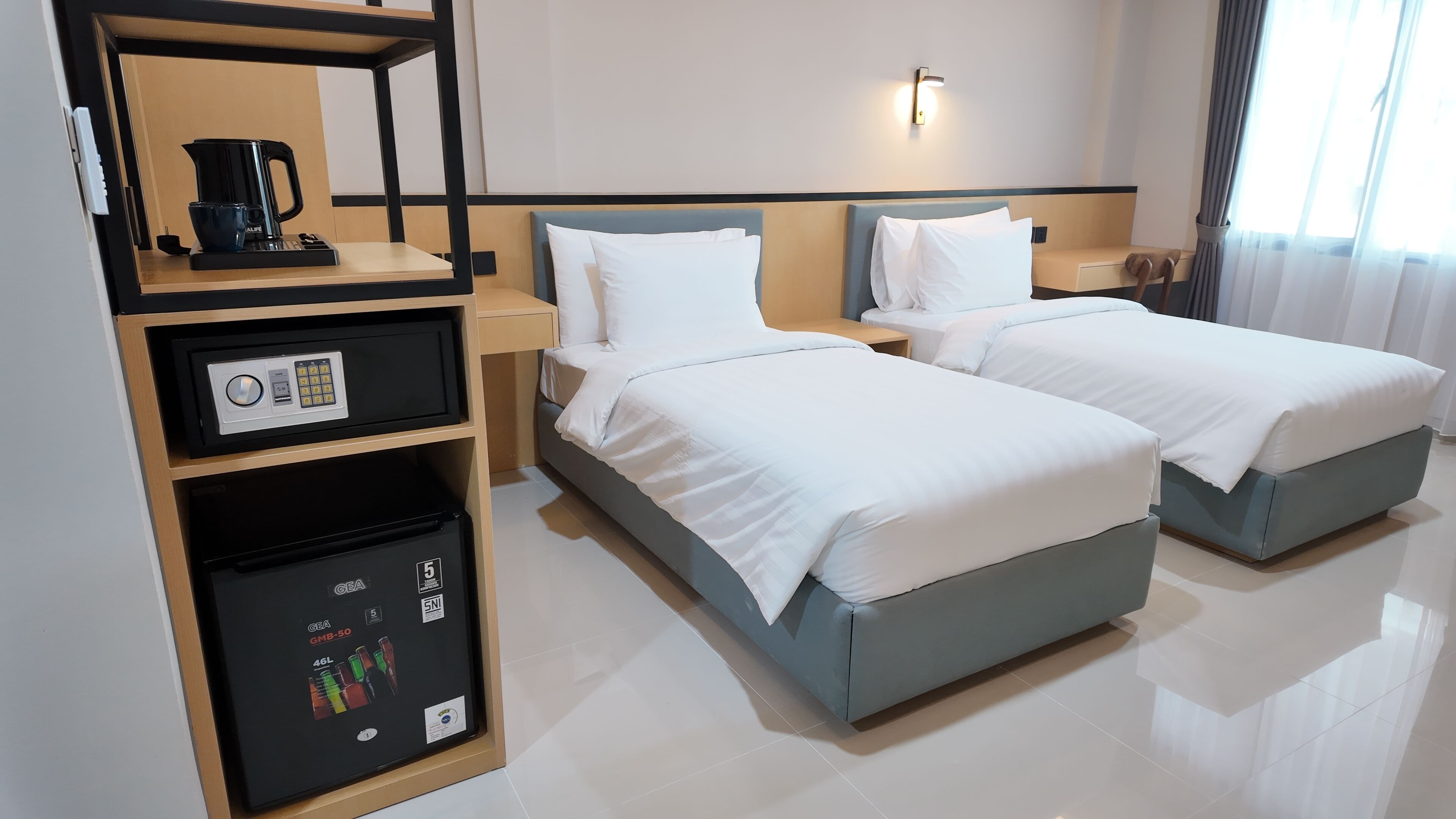 A hotel room with two beds, a minibar, a coffee maker, and a wall-mounted light.