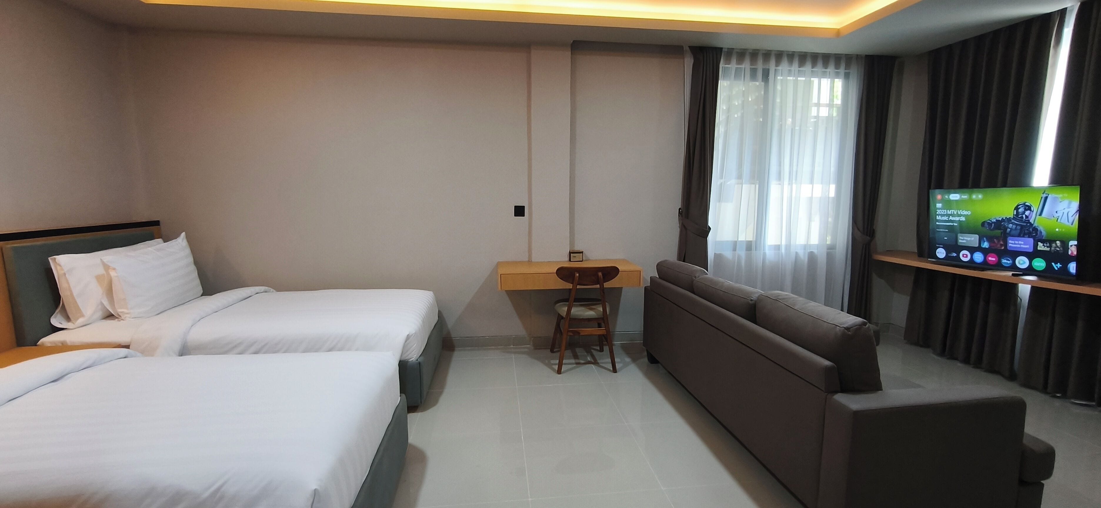 A hotel room with two beds, a desk, a chair, a sofa, and a television.