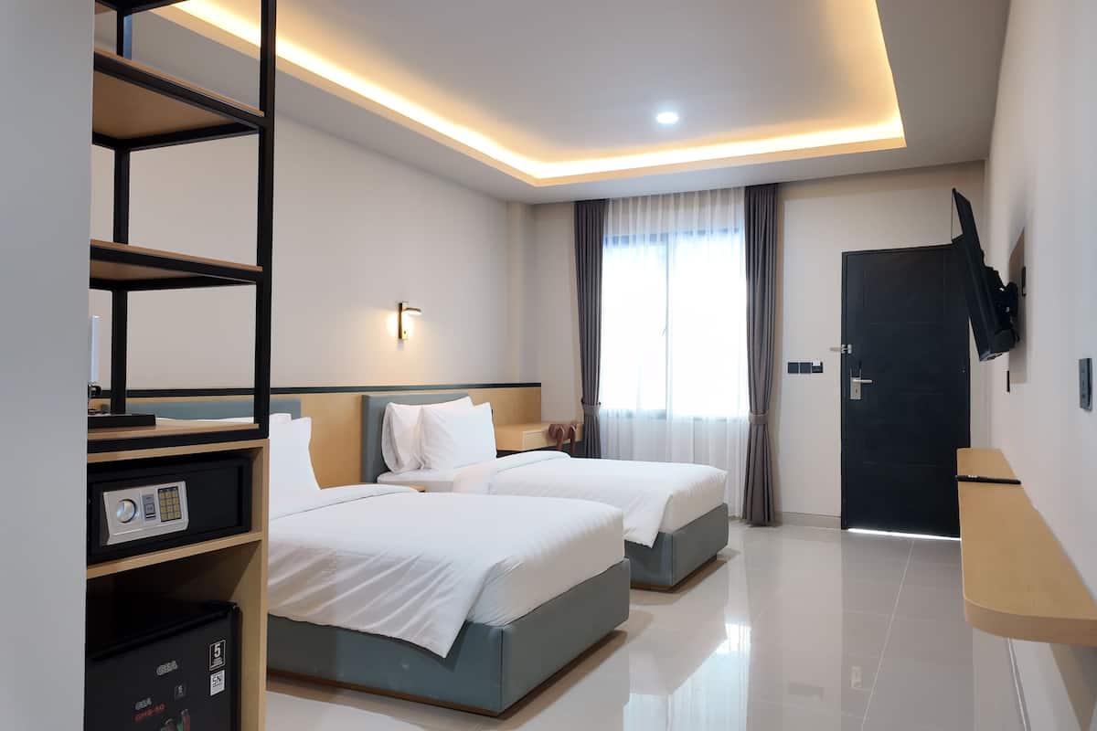 Habitación de hotel con dos camas, un televisor montado en la pared, un escritorio con una computadora y una puerta con manija.