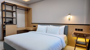 A neatly arranged hotel room with a bed, a bedside table, a shelf unit, and a wall-mounted light fixture. - Mysa Hotel and Co Living (Kuta)