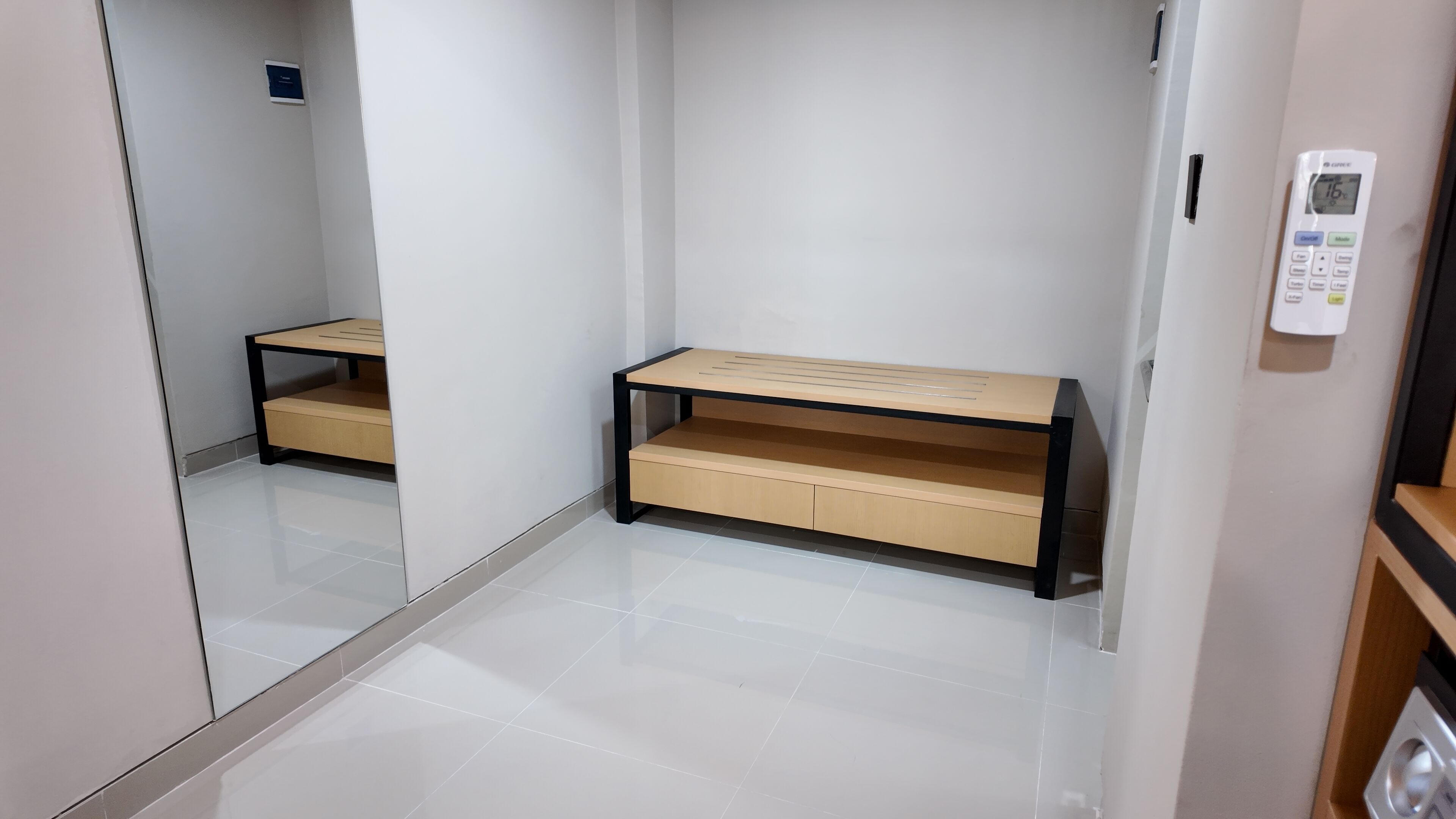 A modern, minimalist room with a wooden bench, a small table, and a wall-mounted control panel.