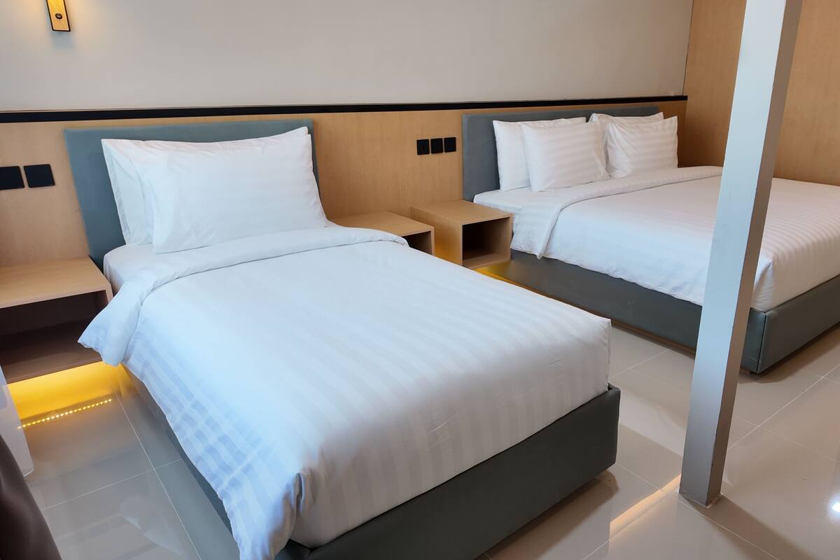 Habitación de hotel con dos camas, una mesita de noche pequeña, una silla y un baño visible a través de una puerta abierta.