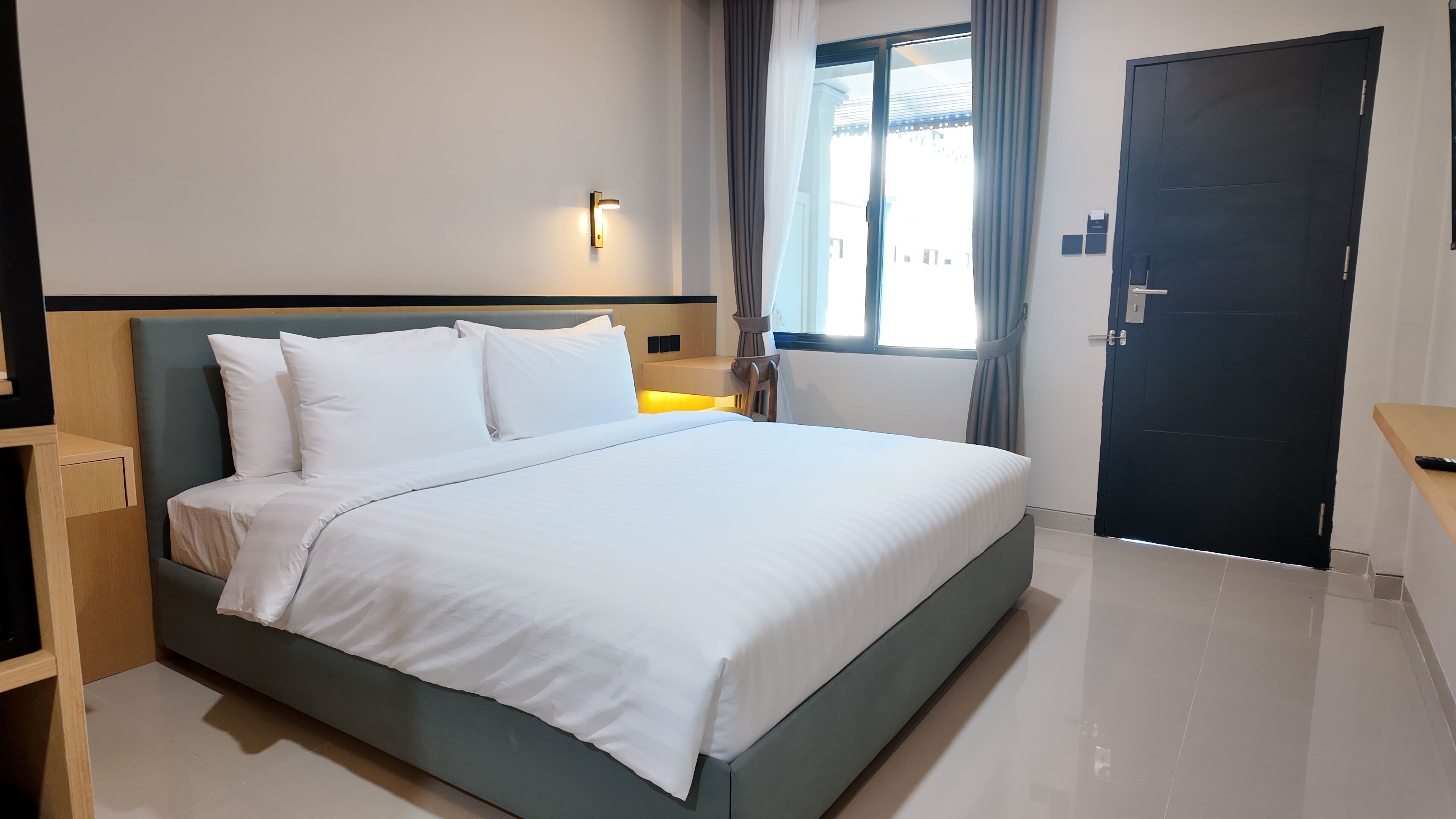 Une chambre d’hôtel avec un lit, une table de chevet, une porte et une fenêtre avec des rideaux.