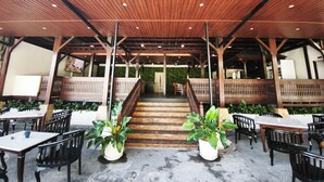An outdoor covered patio area with wooden flooring, tables, chairs, and potted plants. - Casa Mysa Hotel Kuta (Kuta)
