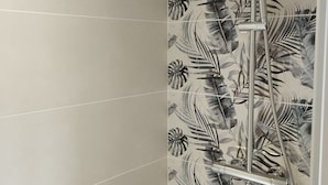 Un baño con ducha, pared con azulejos y cabezal de ducha.