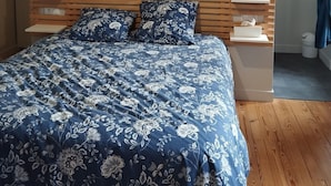Un dormitorio con cabecera de madera, cama con colcha floral, mesitas de noche, lámpara colgante y una lámpara de pared.