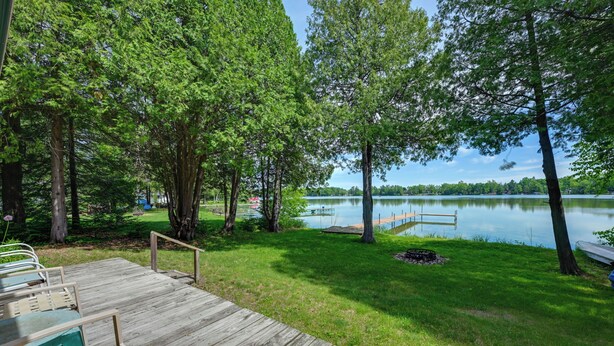 A wooden deck with outdoor seating, a dock extending into a lake, surrounded by trees. - Waterfront Days, Fireside Nights! Lake Helen Haven (Rosholt)