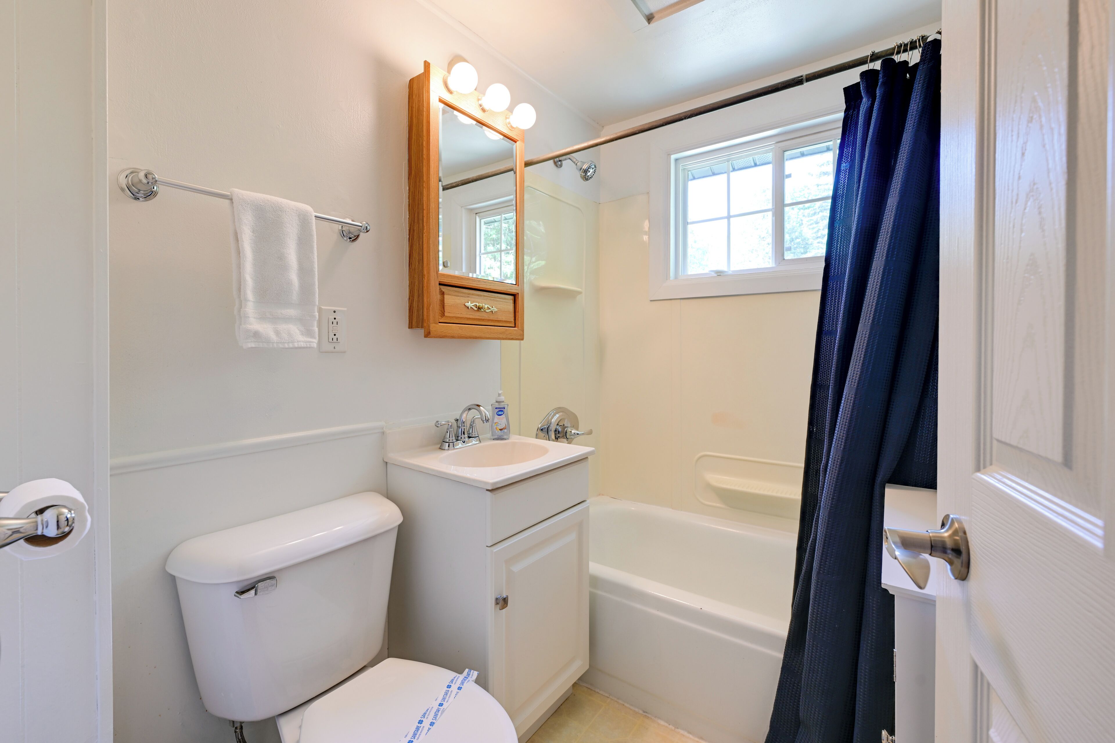 A bathroom with a toilet, sink, mirror, and bathtub.