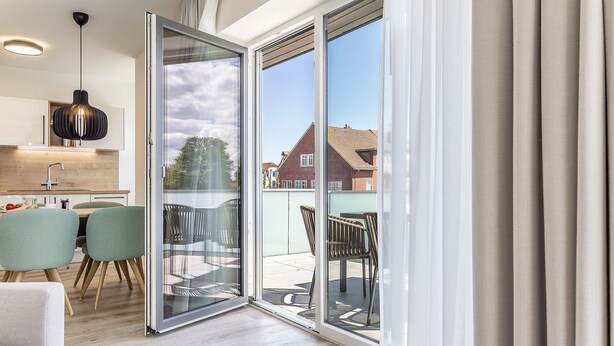 Un apartamento moderno con cocina, zona de comedor y un balcón con mobiliario exterior.
