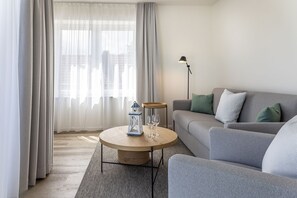 Ein modernes Wohnzimmer mit einem grauen Sofa, einem runden Holztisch und einer Stehlampe.