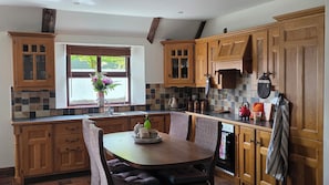 A kitchen with wooden cabinets, a dining table with chairs, a window with a view, and a tiled backsplash. - Thatch cottage historical attractions, medical centre fantastic landscapes (Clonmel)
