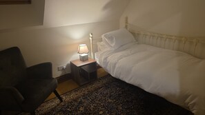 Ett sovrum med en säng, en stol, ett nattduksbord med en lampa och en mönstrad matta.