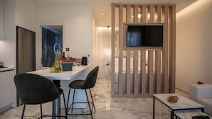 Une cuisine moderne dotée d’un réfrigérateur encastré, d’un coin repas avec un tabouret de bar, d’un téléviseur fixé sur un panneau en bois et d’un sol en marbre.