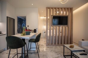 Eine moderne Küche mit einem eingebauten Kühlschrank, einer Essecke mit Barhocker, einem an einer Holzvertäfelung montierten Fernseher und einem Marmorboden.