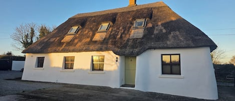 A white cottage with a thatched roof, multiple windows, and a small door.