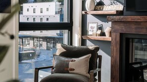 Ein Zimmer mit Blick auf eine verschneite Straße, ein Sessel mit Kissen, ein Regal mit Dekoration und ein Schild mit der Aufschrift 'REVEL STATION'.