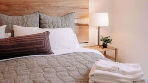 Ein ordentlich bezogenes Bett mit einer gemusterten Decke, Kissen und einem Stapel weißer Handtücher.