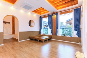 A room with wooden flooring, a bed, a wooden table with chairs, a window with curtains, and a view of traditional architecture. - Modam Stay Gyeongju (Gyeongju-si)