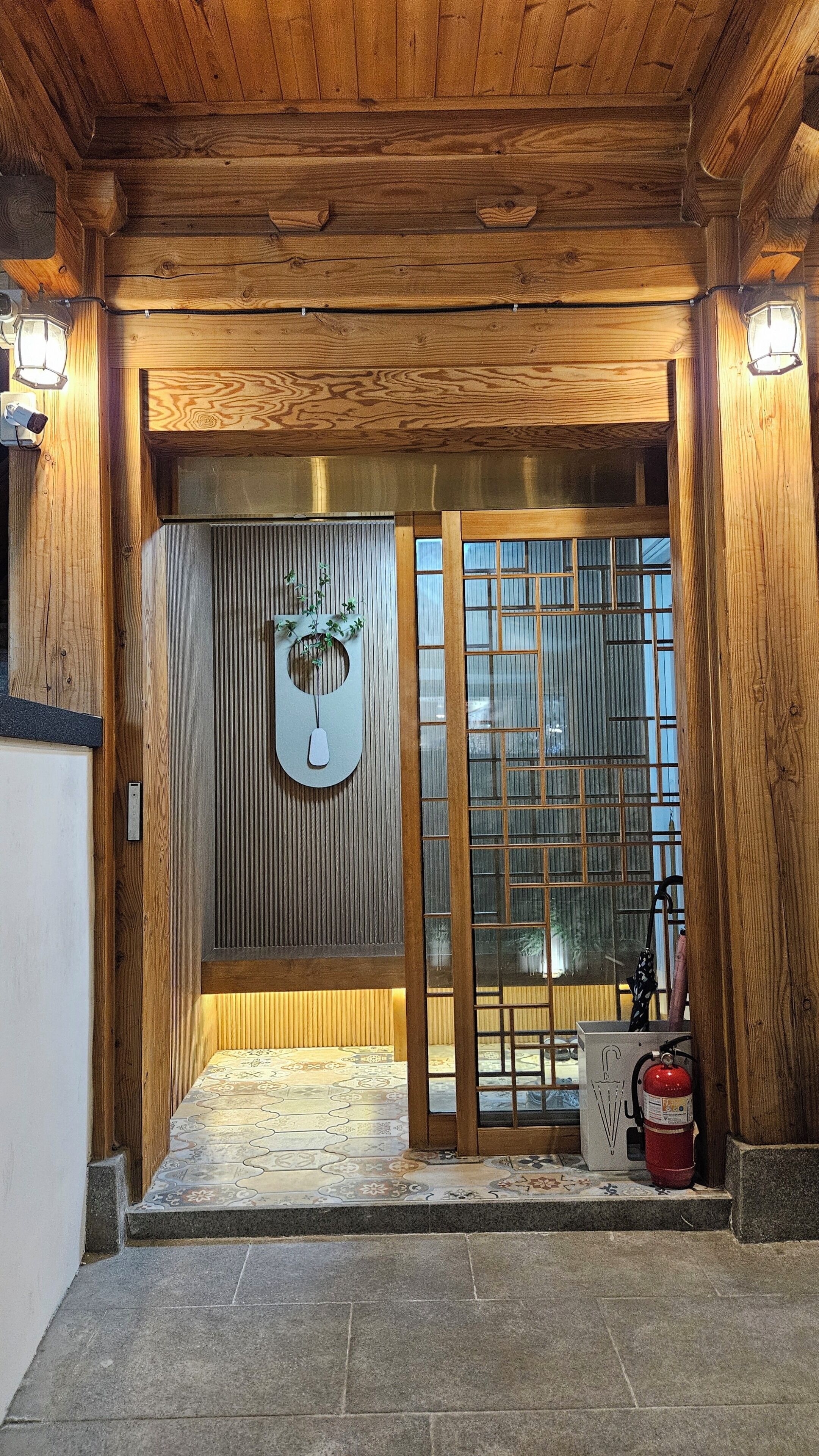 A wooden entrance with a glass door, a fire extinguisher, and a wall-mounted light fixture.