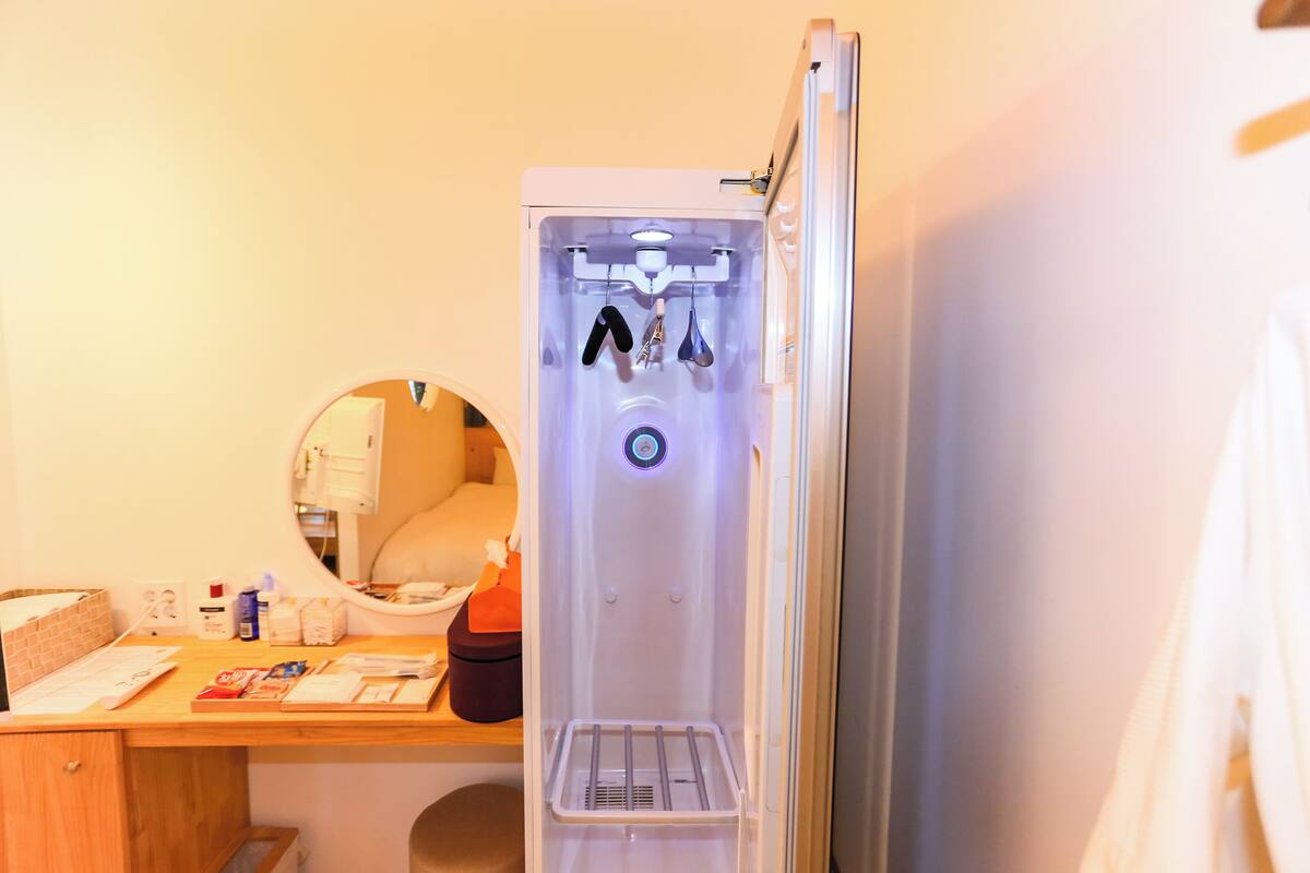 A compact hotel room with a built-in refrigerator, a small wooden desk, and a round mirror.