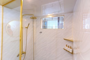 Un baño moderno con cabina de ducha de vidrio, ducha de mano, grifo empotrado en la pared y una pequeña ventana con celosía de metal.