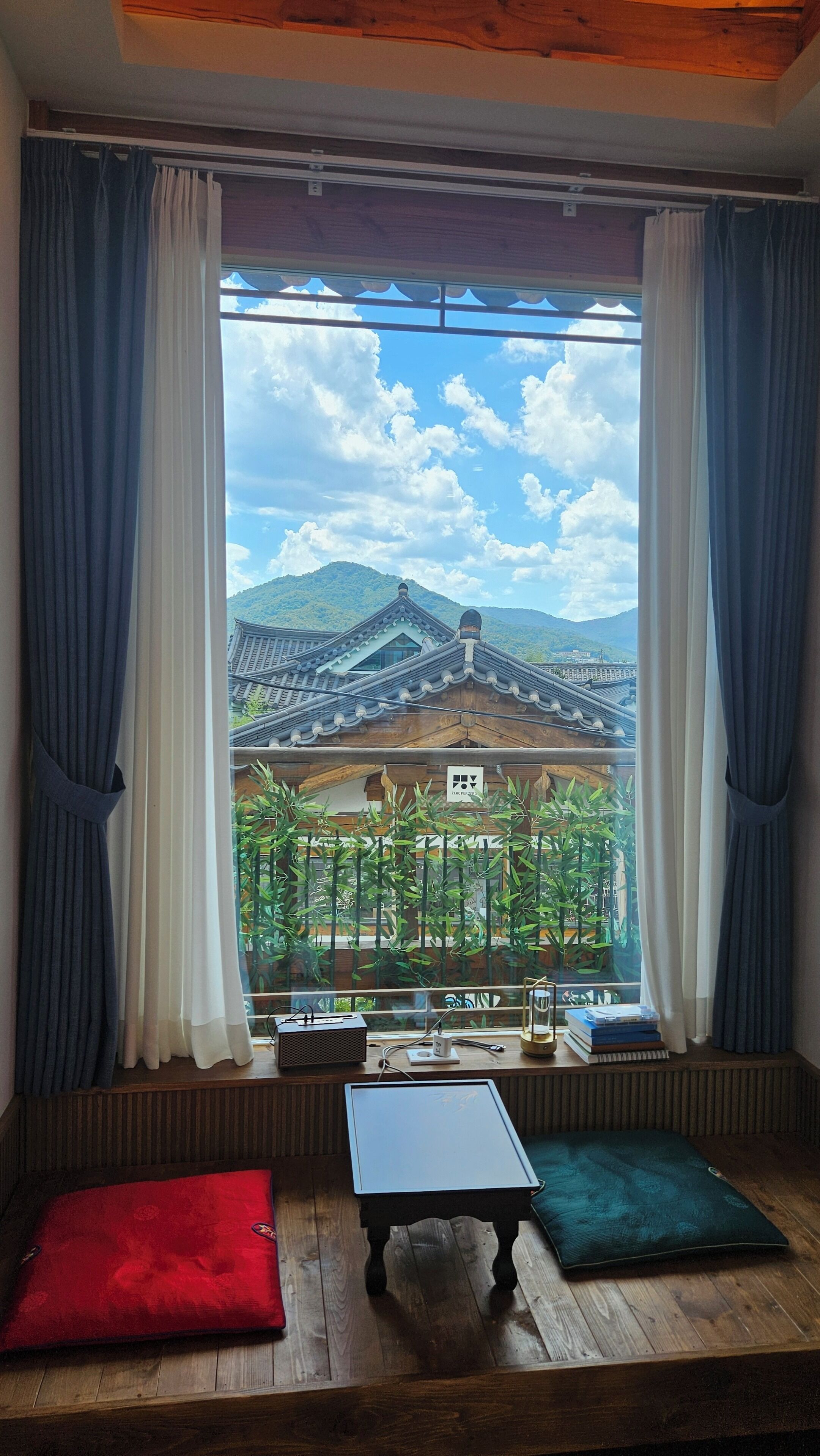 A room with a large window, a small table, and a red pillow.