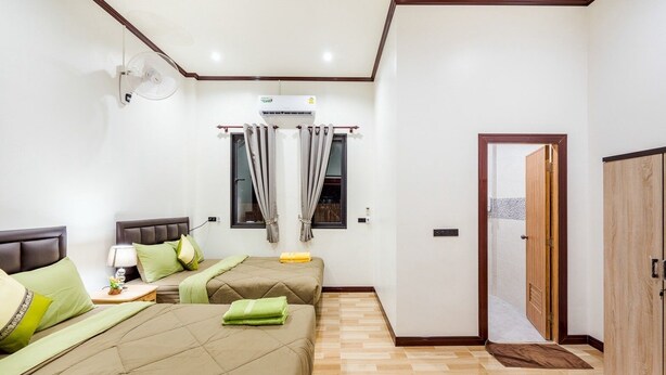 A bedroom with two beds, a bedside table with a lamp, an air conditioning unit, a window with curtains, and a wooden wardrobe. - Baan Hoy Kong Poolvilla (Cha-am)