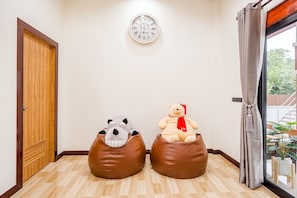 A room with a wooden door, a wall clock, and two bean bags with plush toys. - Baan Hoy Kong Poolvilla (Cha-am)
