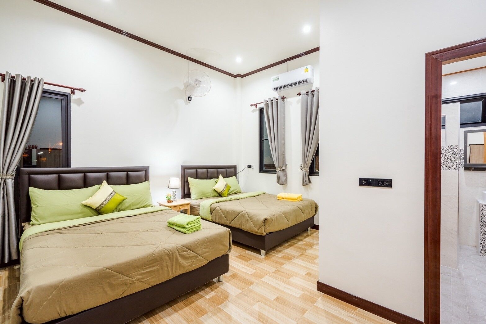 A hotel room with two beds, a ceiling fan, an air conditioning unit, and a wooden floor.