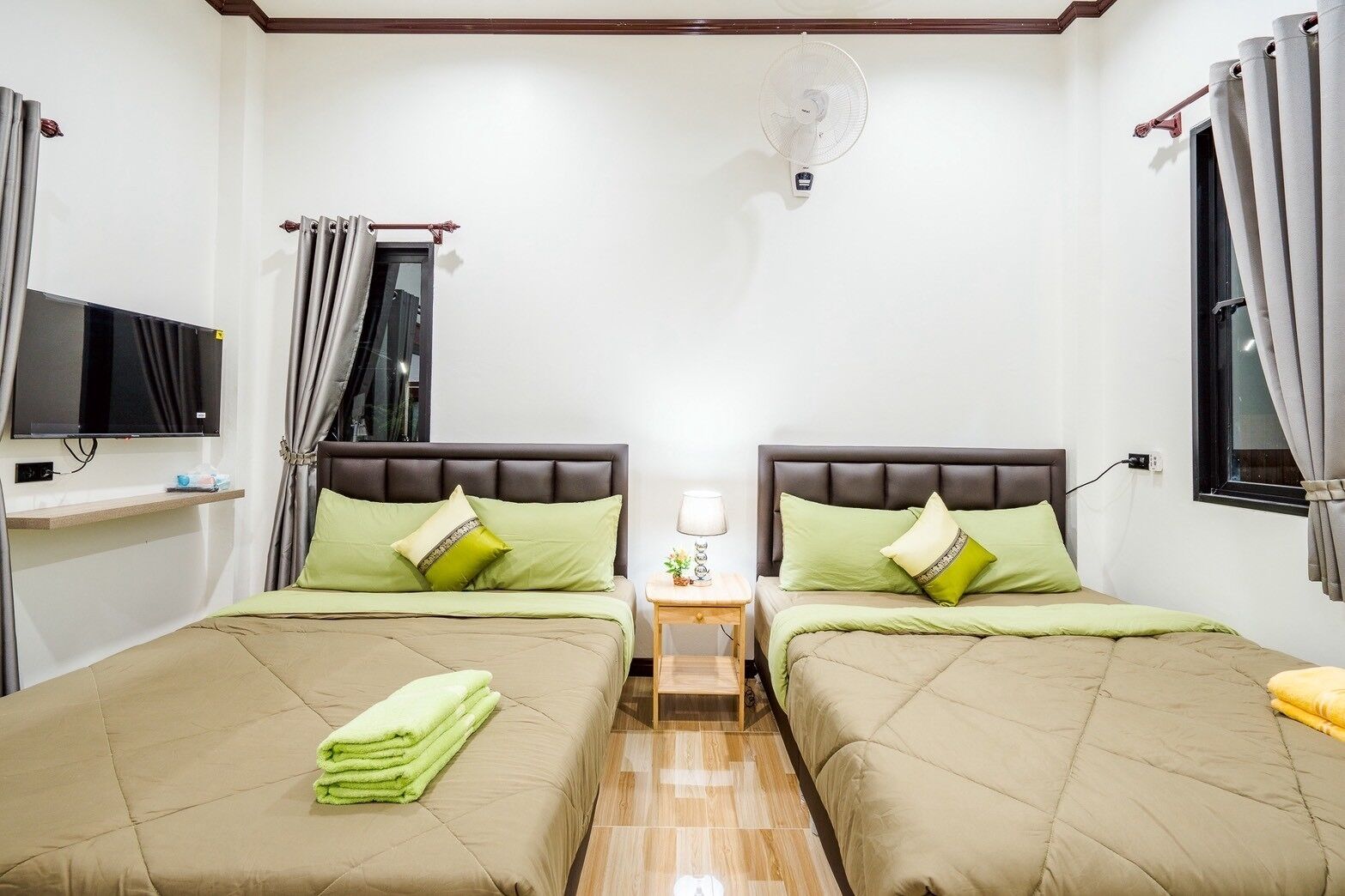 A twin room with two beds, a TV, a bedside table, and a fan.