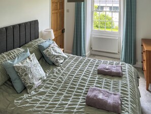 Ein ordentlich bezogenes Bett mit einer gemusterten Bettdecke, zwei Kissen und zwei gefalteten Handtüchern.