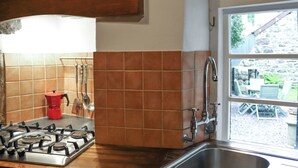 Une cuisine équipée d’une cuisinière à gaz, d’une cafetière rouge et d’une fenêtre donnant sur l’extérieur.