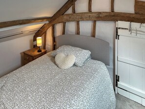 Ein Schlafzimmer mit einem Bett, einem Nachttisch mit Lampe, einem herzförmigen Kopfkissen und einer weißen Tür.