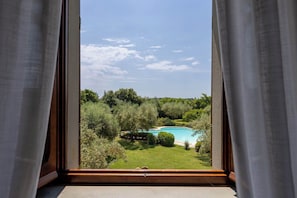 Blick aus dem Fenster auf ein Schwimmbad, umgeben von Grünpflanzen.