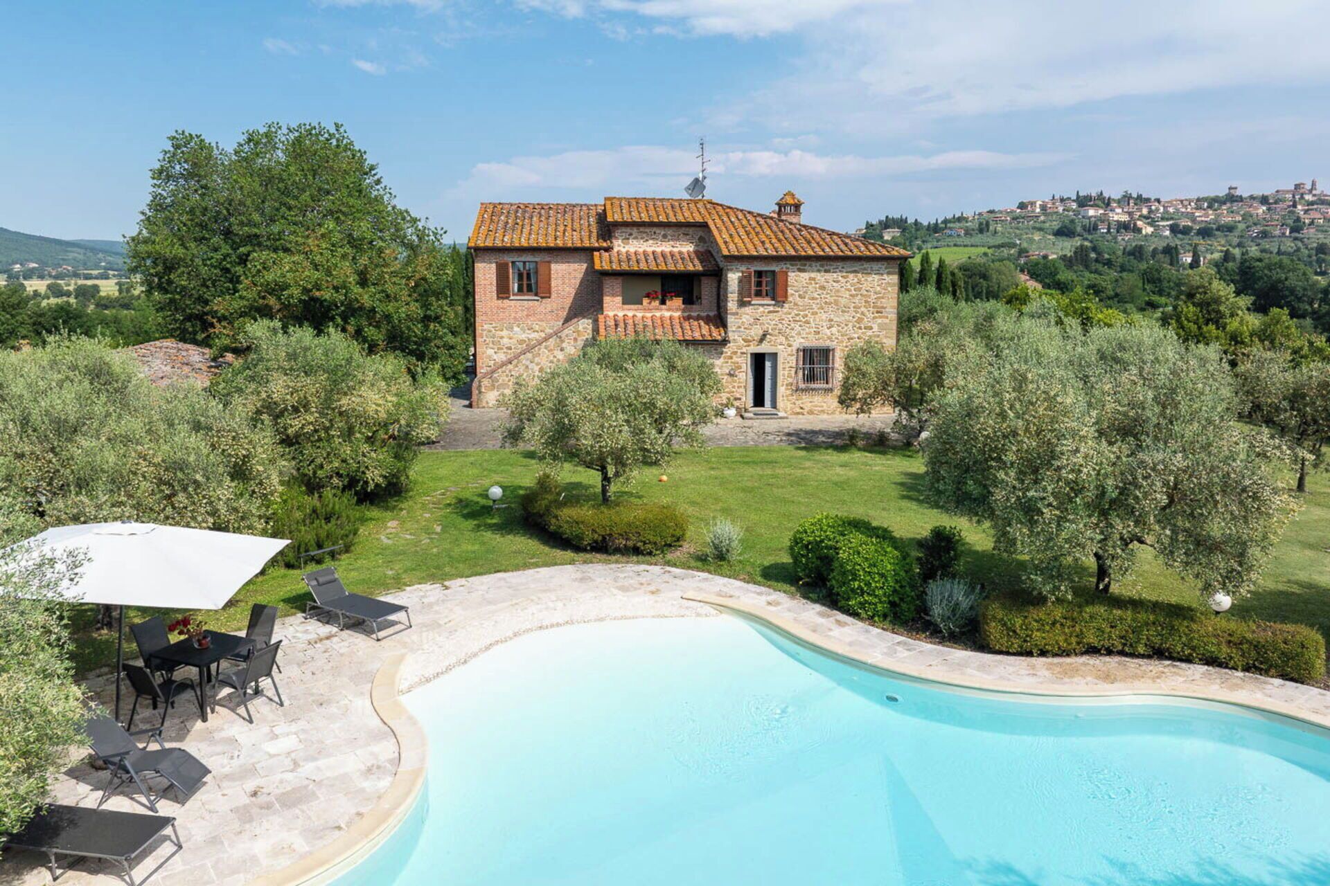 Una casa in pietra con piscina, immersa nel verde e con vista su una cittadina in lontananza.